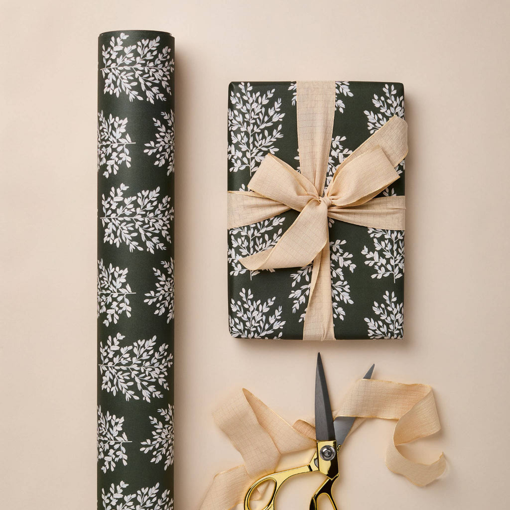 Gift wrapped in black floral paper with a beige ribbon, accompanied by scissors on a beige background.