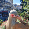 Person with a pink comb with floral design in a park with buildings and trees in the background