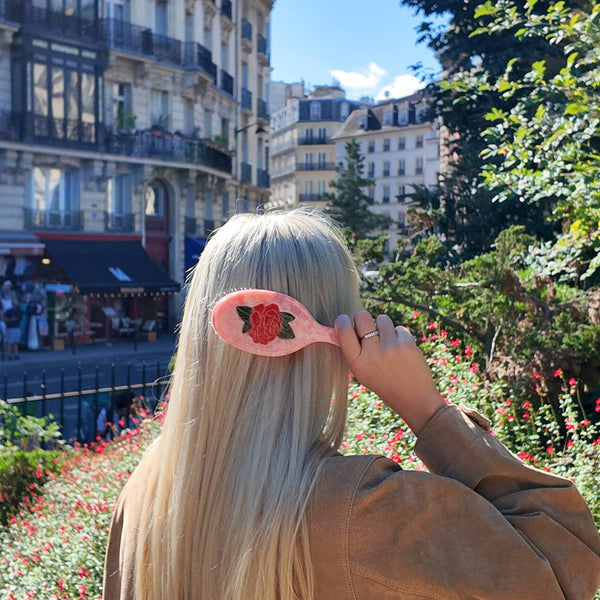 Person with a pink comb with floral design in a park with buildings and trees in the background