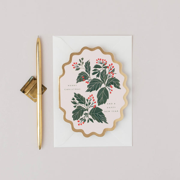 Decorative card with holly design and a pen on a light gray background
