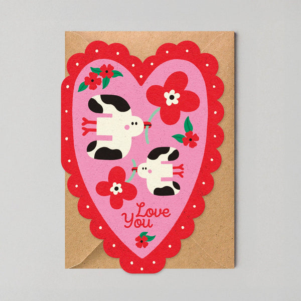Heart-shaped card with cartoon cows and flowers on a gray background