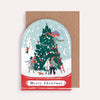 Christmas card with illustration of people decorating a tree inside a snow globe, on a brown envelope.
