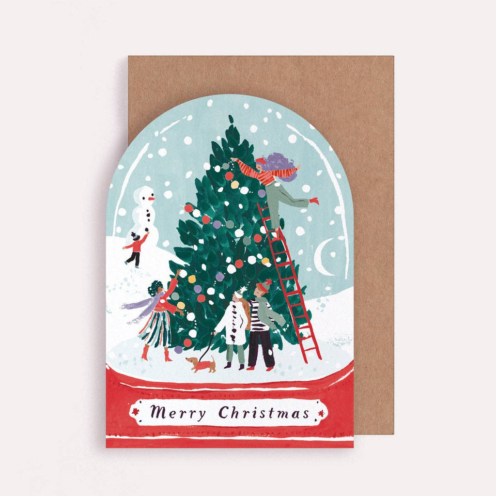 Christmas card with illustration of people decorating a tree inside a snow globe, on a brown envelope.