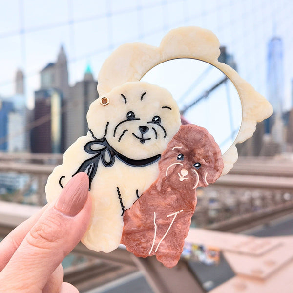 Two small plush toys, one white with black face and the other brown, held against a cityscape background.