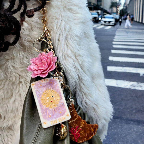 Keychain with charms attached to a green bag on a city street