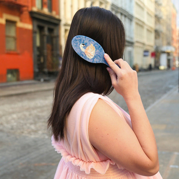 Woman in a pink dress combing her hair with a decorative comb on a city street.