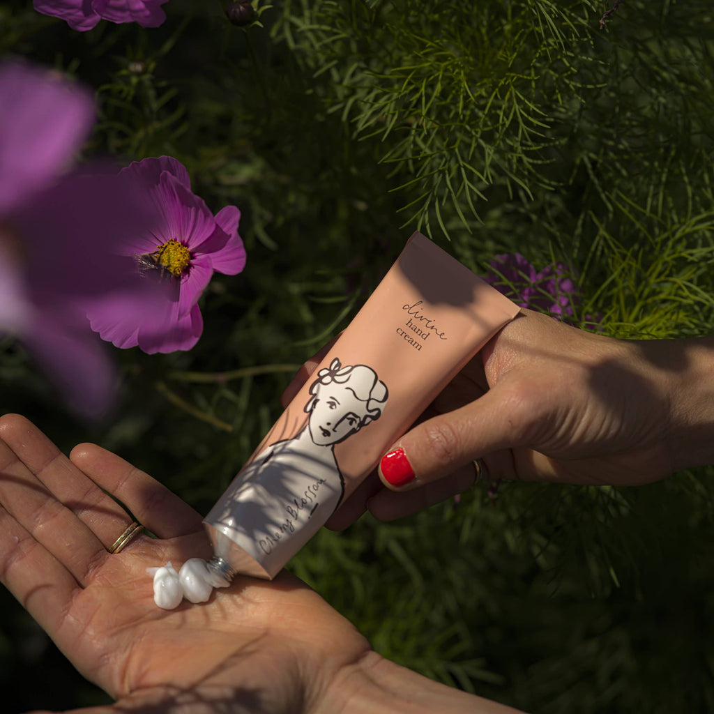 Hand applying cream from a tube with a cartoon character on a background of greenery and flowers.