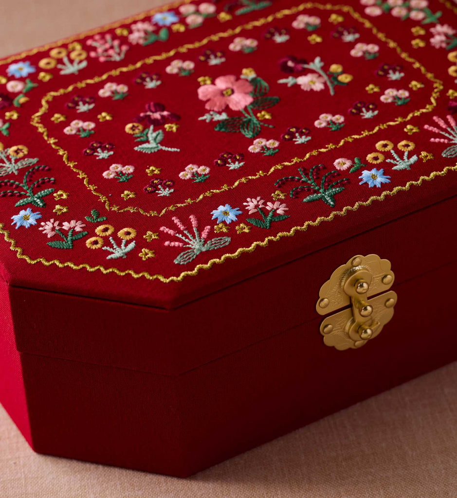 Red embroidered box with floral patterns and a gold clasp on a beige surface