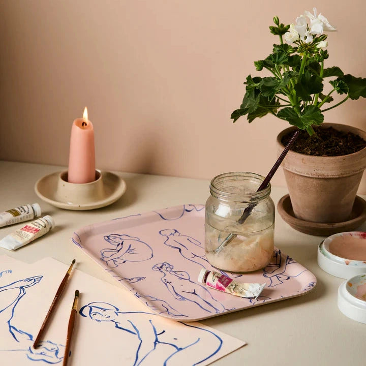 Artistic setup with a candle, plant, and art supplies on a table against a beige wall.