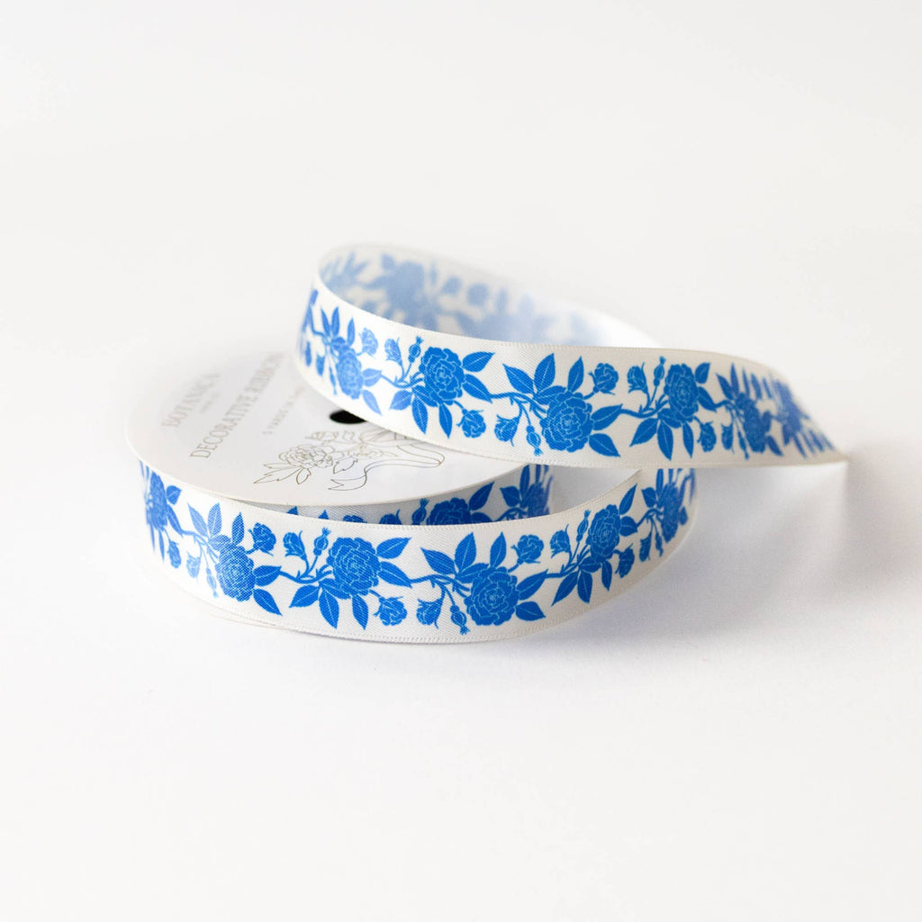 A roll of white ribbon with a repeating blue floral pattern, coiled on a clean white background.