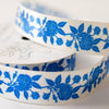 A close-up of a white ribbon with a repeating blue floral pattern, coiled on a light neutral background.