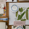 Stationery items including a notebook with plant illustrations, sticky notes, and decorative tape on a wooden surface.
