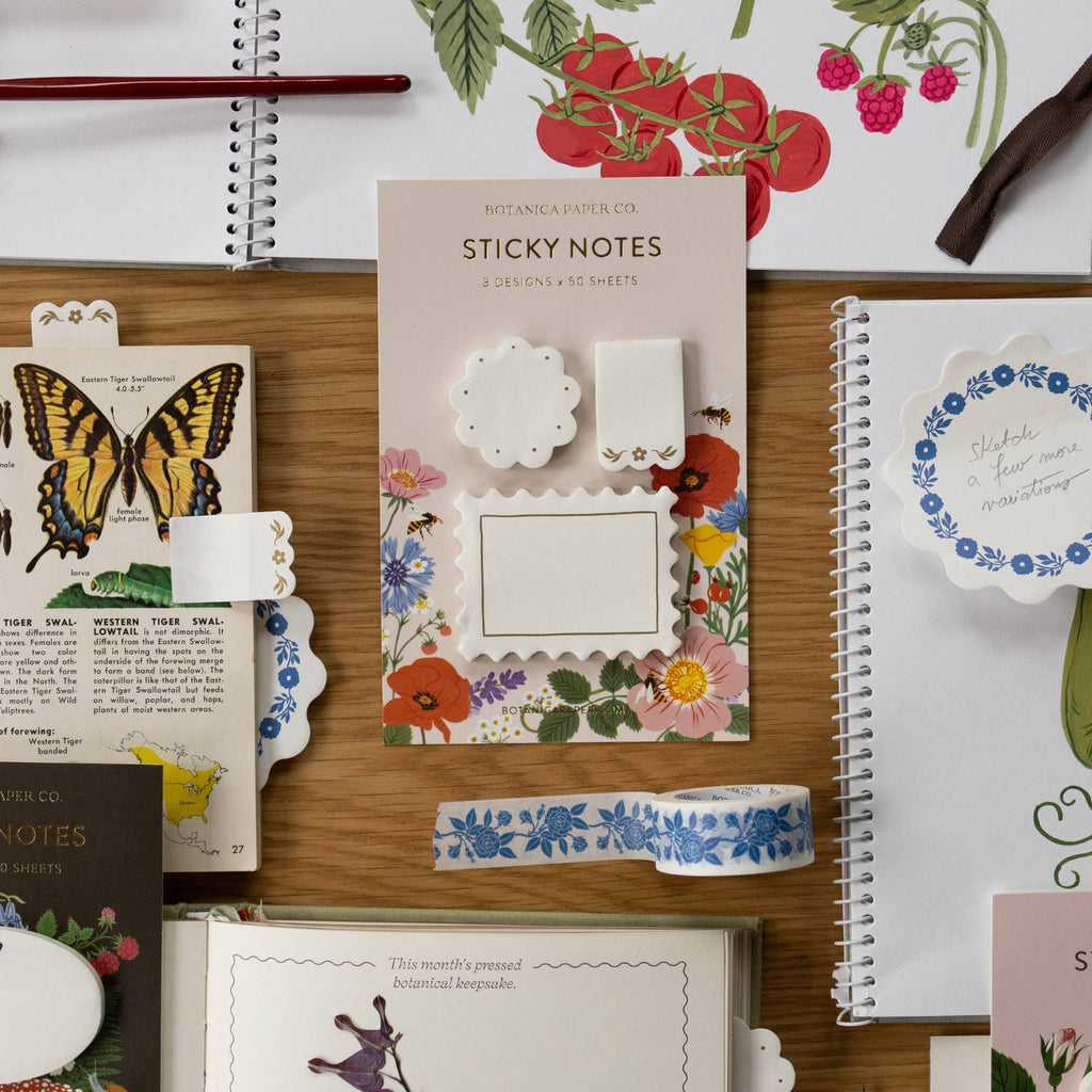 Floral sticky notes and decorative items on a wooden surface with stationery items.
