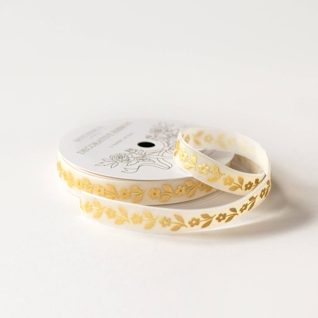 A spool of decorative washi tape with a delicate gold floral pattern on a white background, photographed on a clean white surface.