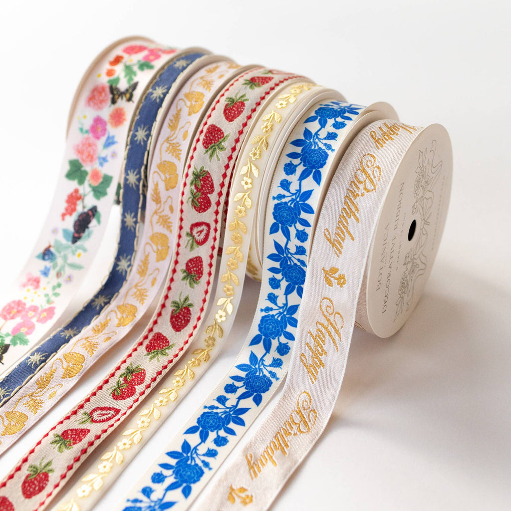 A set of decorative ribbon spools with colorful floral and fruit patterns, including strawberries, blue flowers, and gold foil lettering, arranged on a clean white background.