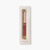 A Botanica pen with a rose gold cap and a terracotta brown barrel, presented inside its cream-colored packaging box against a light gray background.