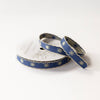 A spool of decorative ribbon with a navy blue base and a repeating pattern of gold snowflakes and scalloped edges, shown on a clean white background.