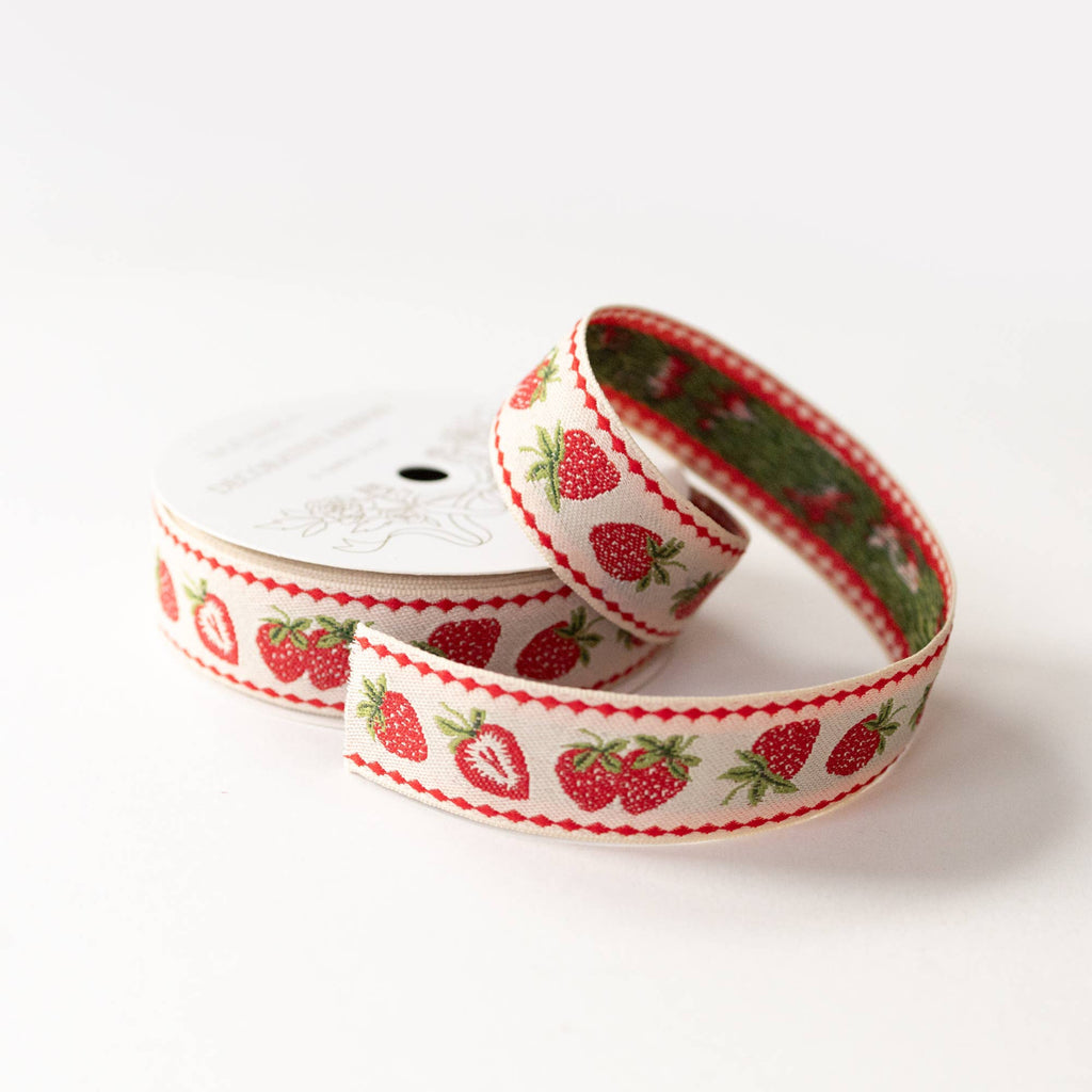 A roll of white ribbon printed with red strawberries and green leaves, with a red diamond border, shown on a white background.