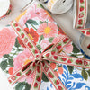 A gift-wrapped package tied with a matching ribbon, featuring a colorful floral and strawberry print. Rolls of coordinating ribbon are partially visible around it on a light surface.