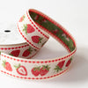 A close-up of a spool of grosgrain ribbon featuring a red and green strawberry pattern on a white background, with a red dotted border.