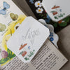 Card with 'Common Blue Butterfly' illustration on a book page with botanical illustrations.