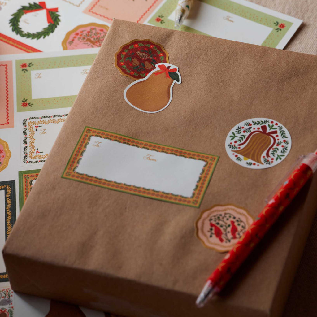 Brown paper package with decorative stickers on a surface with more paper and a pen.