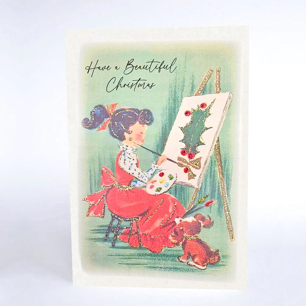 Vintage-style Christmas card with a woman painting a Christmas tree, accompanied by a dog.