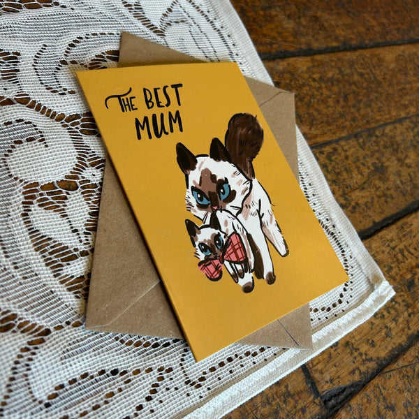 Greeting card with illustration of two cats and 'The Best Mum' text on a lace tablecloth.