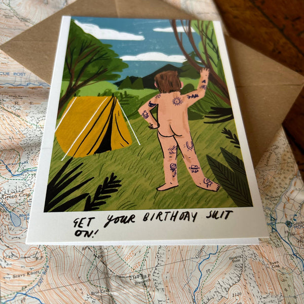 Illustrated birthday card with a person by a tent in a forest, on a map background.