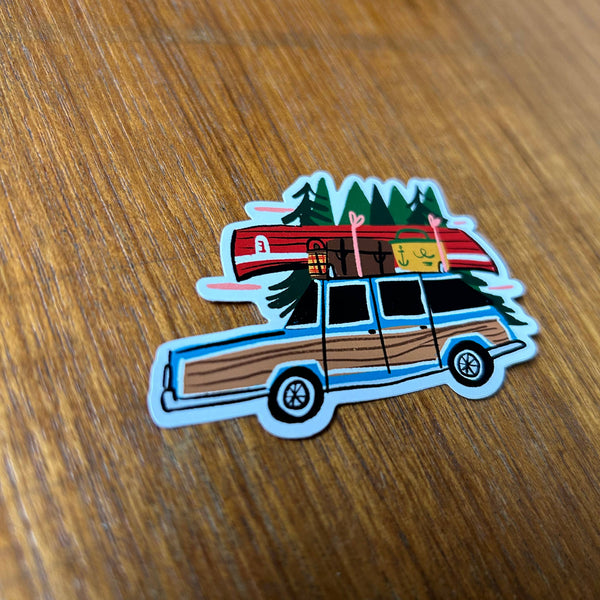 Sticker of a vintage station wagon with camping gear on a wooden surface