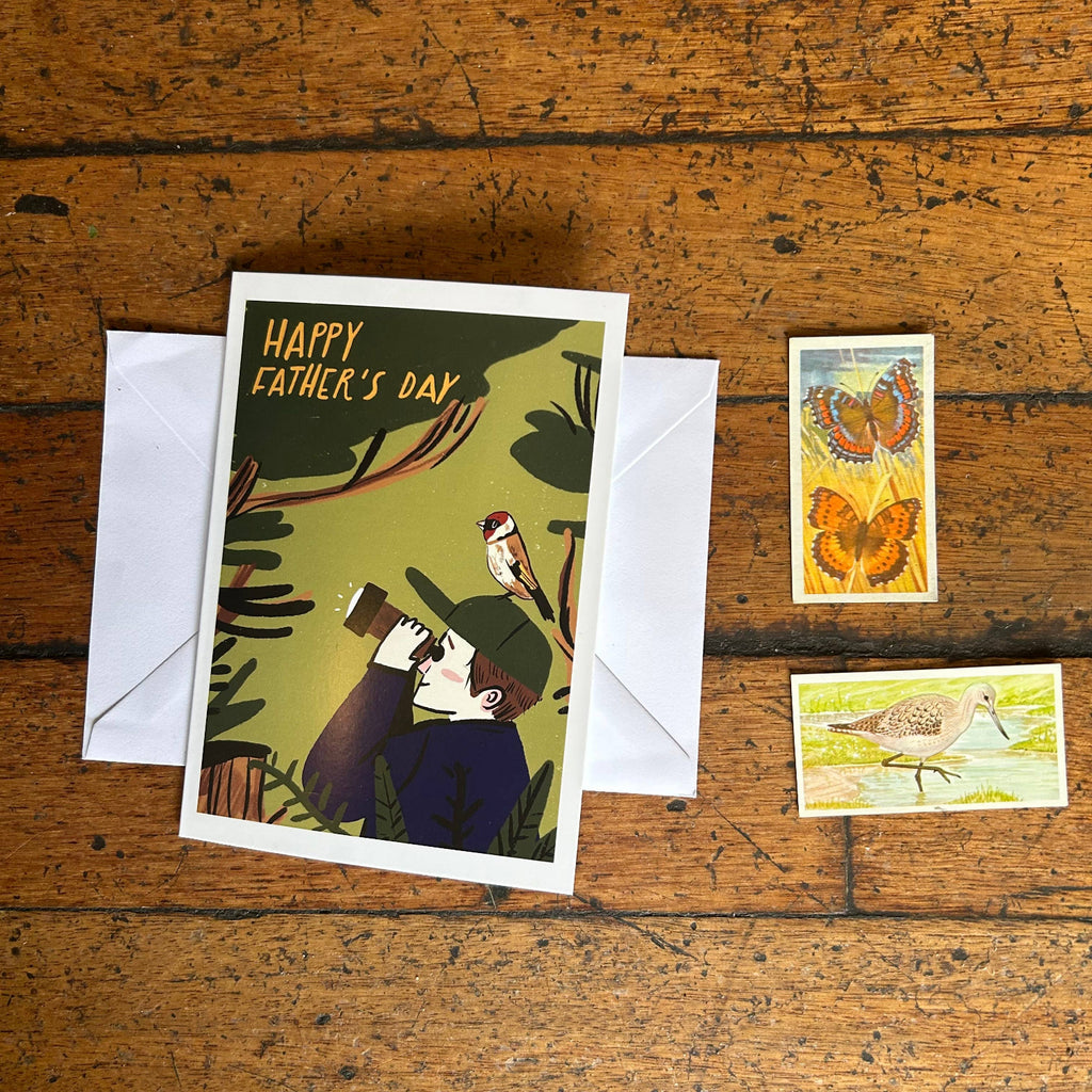 Father's Day card with a child and bird illustration on a wooden surface with stamps.