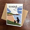 Greeting card with illustration of a silhouette of a person holding a child, set against a landscape with mountains and birds, on a wooden surface.