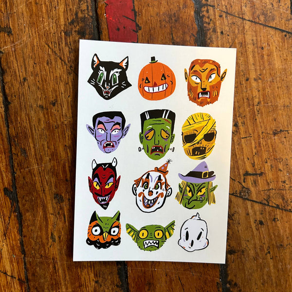 Sheet of Halloween-themed stickers with various character faces on a wooden surface.
