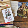 Card with 'Happily Ever After' text on a wooden surface with a castle postcard and fabric.