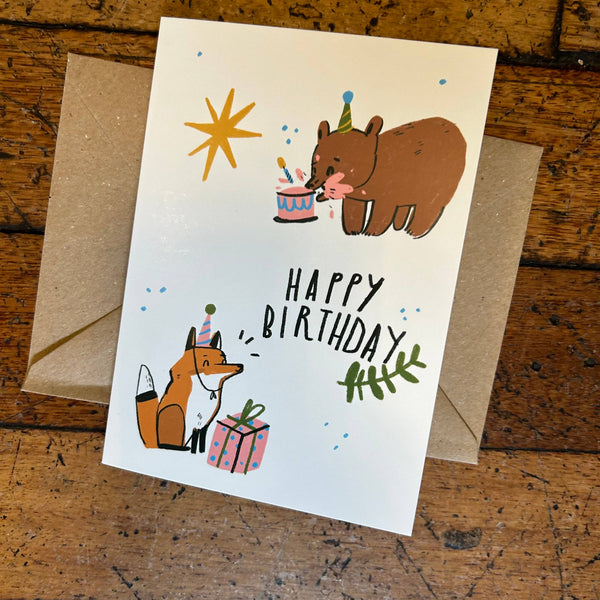 Birthday card with bear and fox illustration on a wooden surface