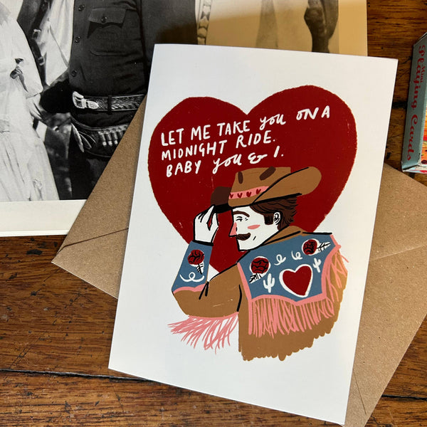 Card with cowboy illustration and heart-shaped text on a wooden surface