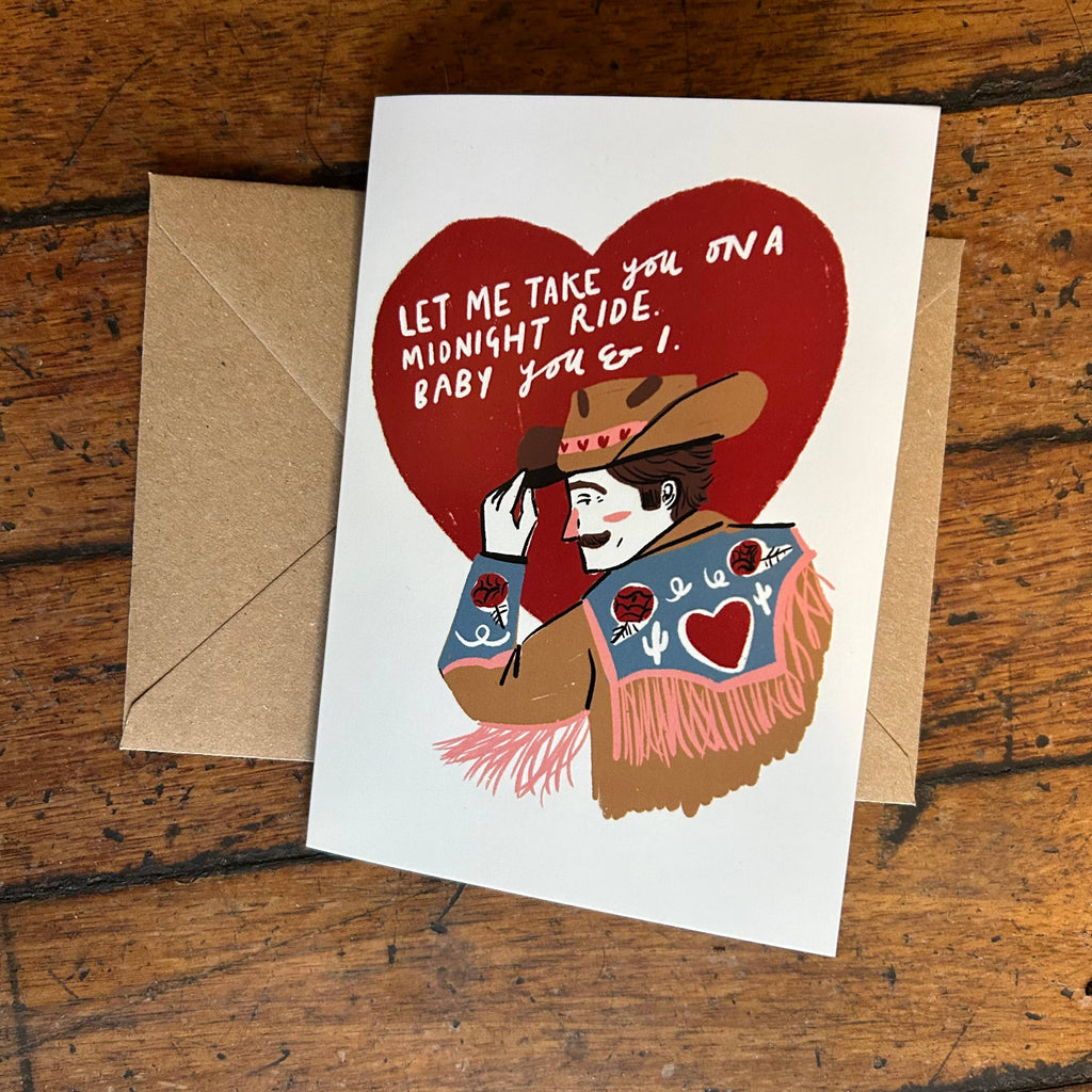 Greeting card with cowboy illustration and heart-shaped text on a wooden surface