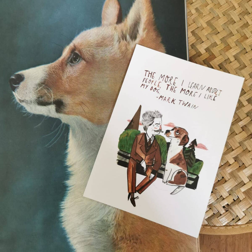 Postcard with a dog illustration and Mark Twain quote next to a painting of a dog on a wooden surface.
