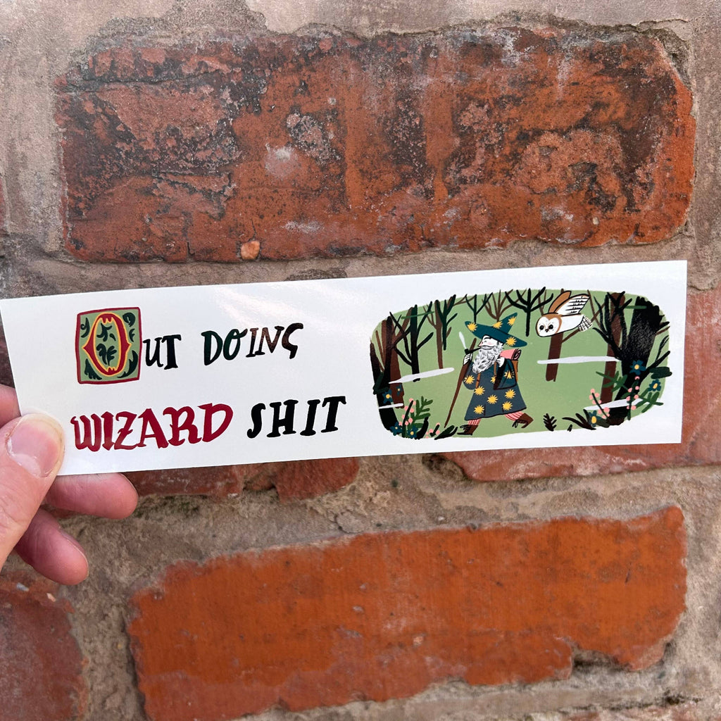 Hand holding a sticker with text and graphics against a brick wall background