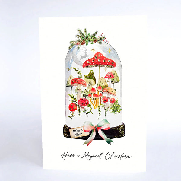 Christmas card with mushrooms, a reindeer, and a bow inside a glass dome on a light blue background.