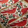 Close-up of a white embroidered textile featuring large red birds, green leaves, pink flowers, and gold decorative trim.