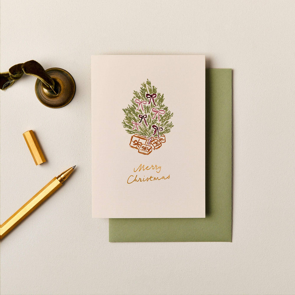 Luxury A6 Christmas card with gold foil text, illustrated tree with pink bows, and a soft green envelope on textured paper.