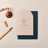 Cream-colored arched Christmas card with gold foil typography and dots, featuring a textured finish and dark envelope.