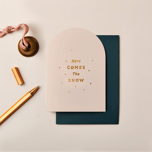 Cream-colored arched Christmas card with gold foil typography and dots, featuring a textured finish and dark envelope.