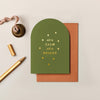 Olive green arched Christmas card with gold foil text and stars, textured cardstock, and a rust-colored envelope.