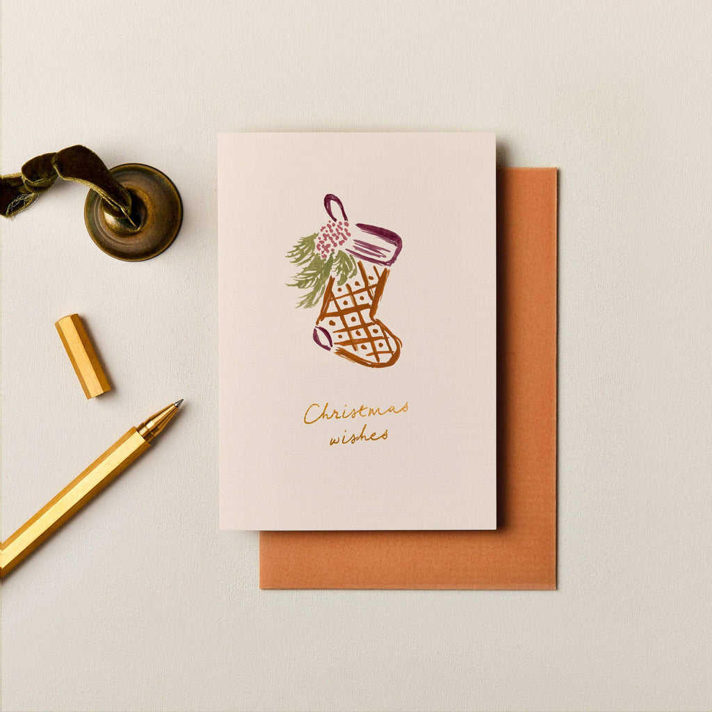 Textured A6 Christmas card with gold foil stocking illustration and envelope on a neutral background.