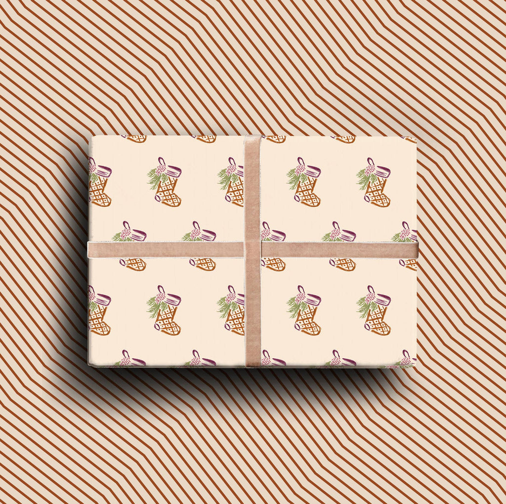 Double-sided Christmas gift wrap featuring hand-painted stockings on cream paper with a rust chevron reverse pattern.