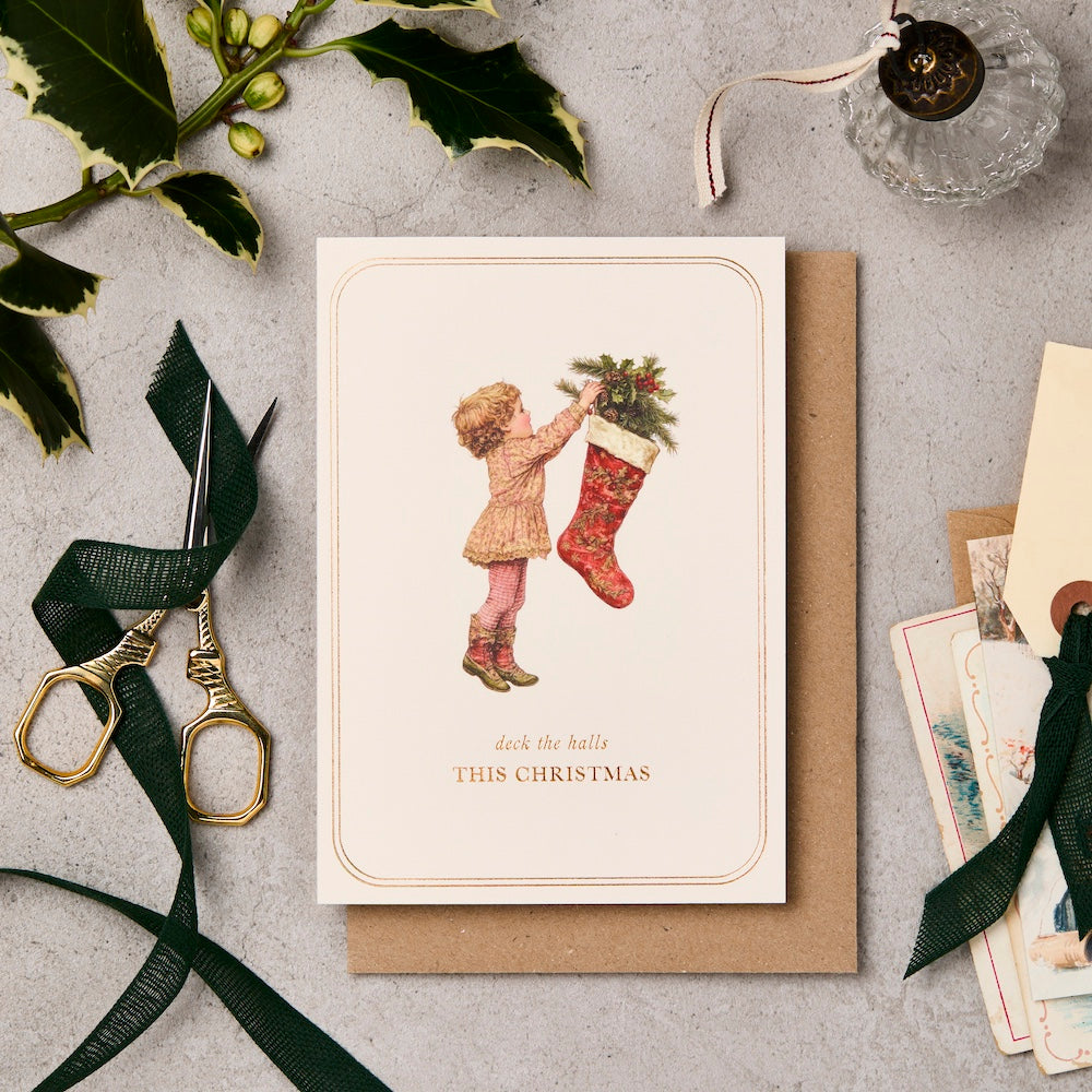 Christmas card with a child and stocking, surrounded by festive items on a textured surface.