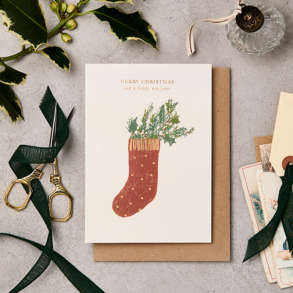 Christmas card with a stocking design on a gray surface with decorative items.