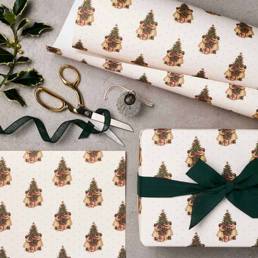 Gift wrap with Christmas tree design, scissors, and ribbon on a gray surface.